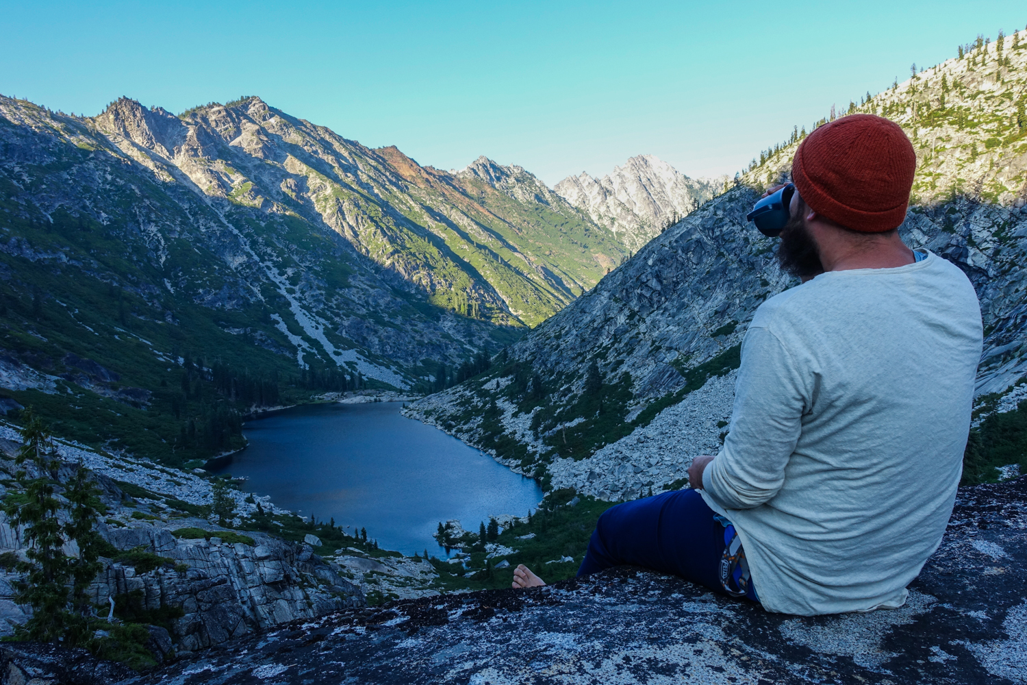 camper in the trinity alps drinking coffee in the morning overlooking an alpine lake and its surrounding mountains 
