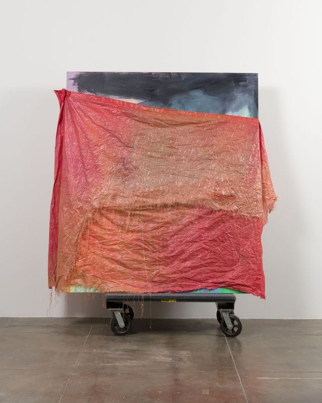 Abstract painting partially covered by a red translucent fabric on a rolling cart.