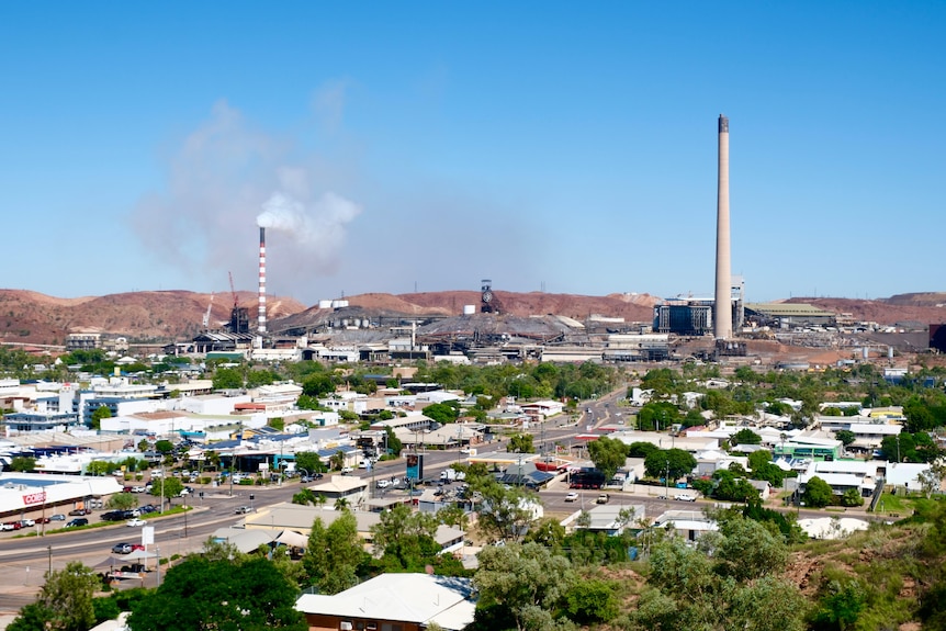 A landscape view of an outback town in the midday sun, with industrial stacks in the background