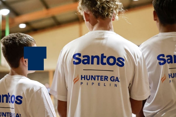 Young people stand together wearing white T-shirts with words including Santos written on the back in blue.