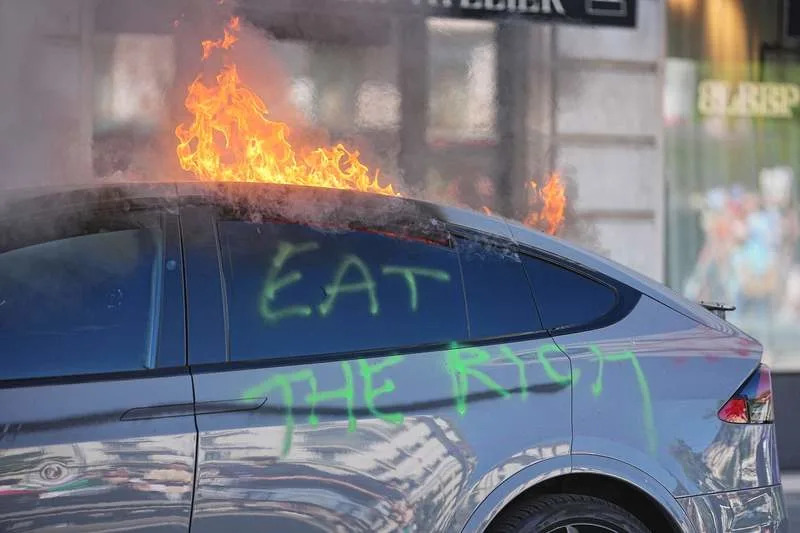 A Tesla Model 3 is seen on fire with the words “Eat the rich” painted on its side during a demonstration organised by the “No-G7” coalition of more than 60 associations, trade unions and left-wing groups a day ahead of the G7 summit, as protesters voice opposition to what they describe as fascism and imperialism. (is associated with: «Swiss police surround violent rioters amid anti-G7 protest in Geneva») Michael Kappeler/dpa