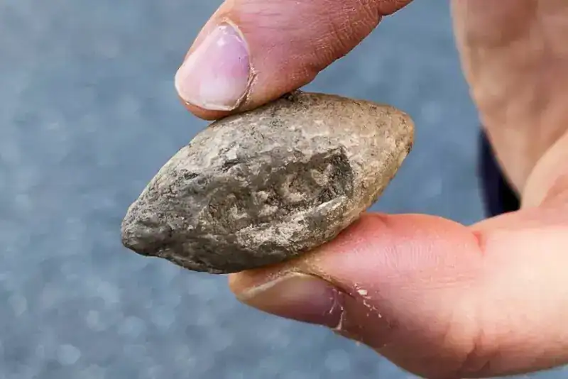 A lead slingshot, an oblong piece of rounded metal, being held up for the camera
