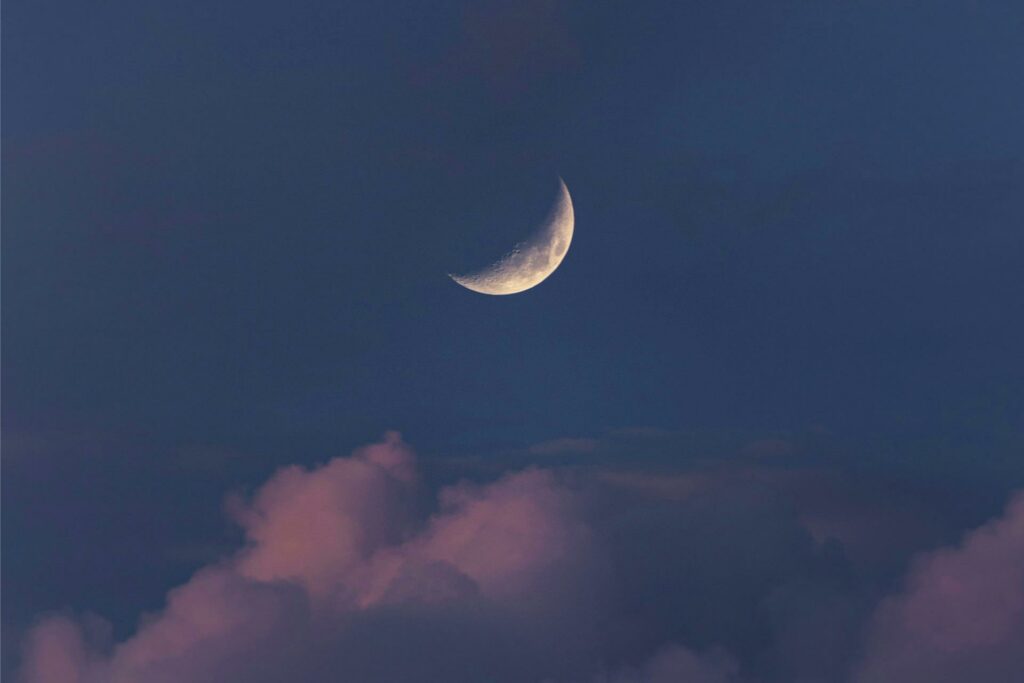 Eine Sichel des Mondes ist am Abendhimmel über einer Wolke zu sehen.