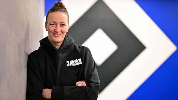 Almuth Schult lehnt vor einem HSV-Logo an der Wand. © Witters 