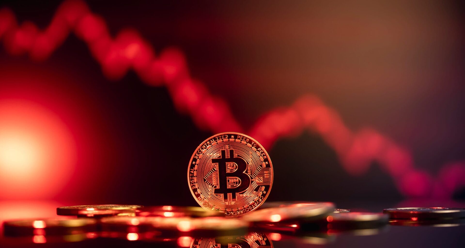 Eine Bitcoin-Münze liegt auf einer reflektierenden Oberfläche, im Hintergrund zeichnet sich ein rotes, nach unten gerichtetes Liniendiagramm ab, das einen kürzlichen Rückgang des Wertes der Kryptowährung signalisiert.
