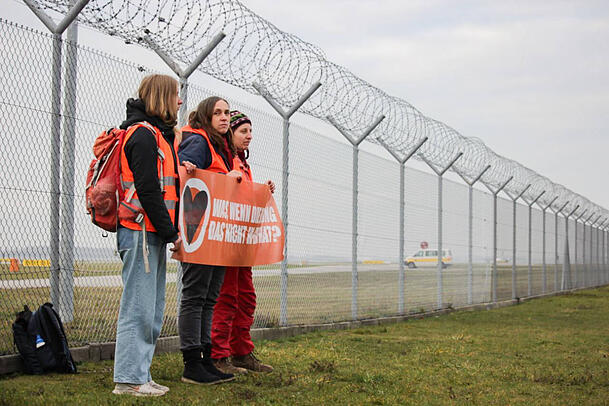 Die Letzte Generation demonstriert vor dem Rollfeld des Münchner Flughafens.