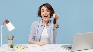 Symbolbild theoretische Führerscheinprüfung mit neuen Fragen vom 1. April 2025: Frau hält lachend einen Autoschlüssel in der Hand