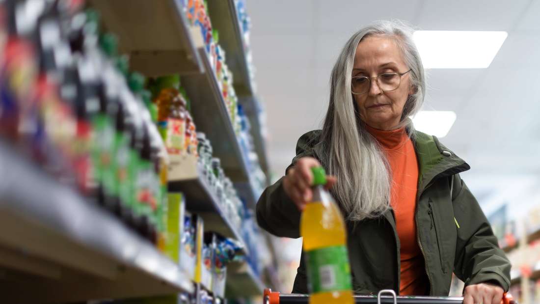 Frau legt Getränk in Einkaufswagen