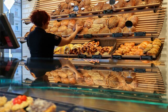 Eine Frau nimmt ein Brot aus einem Regal in einer Bäckerei.