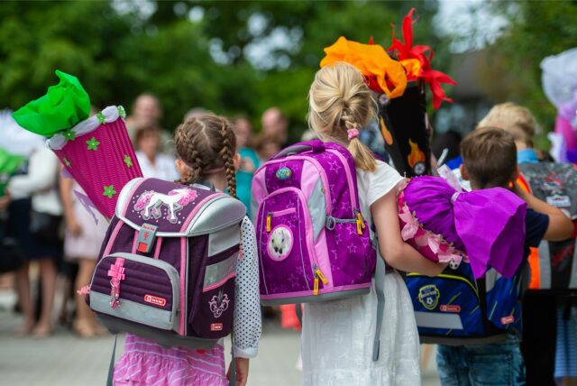 Mädchen und Jungen mit Schultornistern und Schultüten drehen der Kamera den Rücken zu.