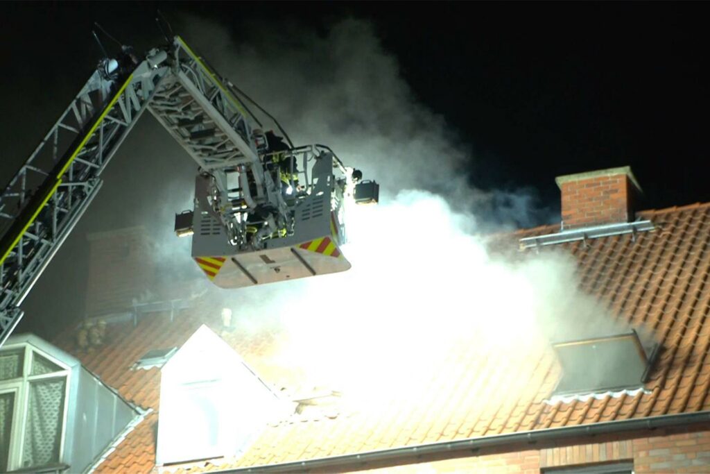 Der Korb einer Drehleiter neben dem rauchenden Dach des Hauses in Dortmund, in dessen Tiefgarage der Brand ausgebrochen war.