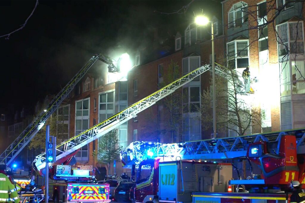Drei Drehleiterwagen der Feuerwehr stehen vor dem Haus in Dortmund, in dessen Tiefgarage der Brand ausgebrochen war.
