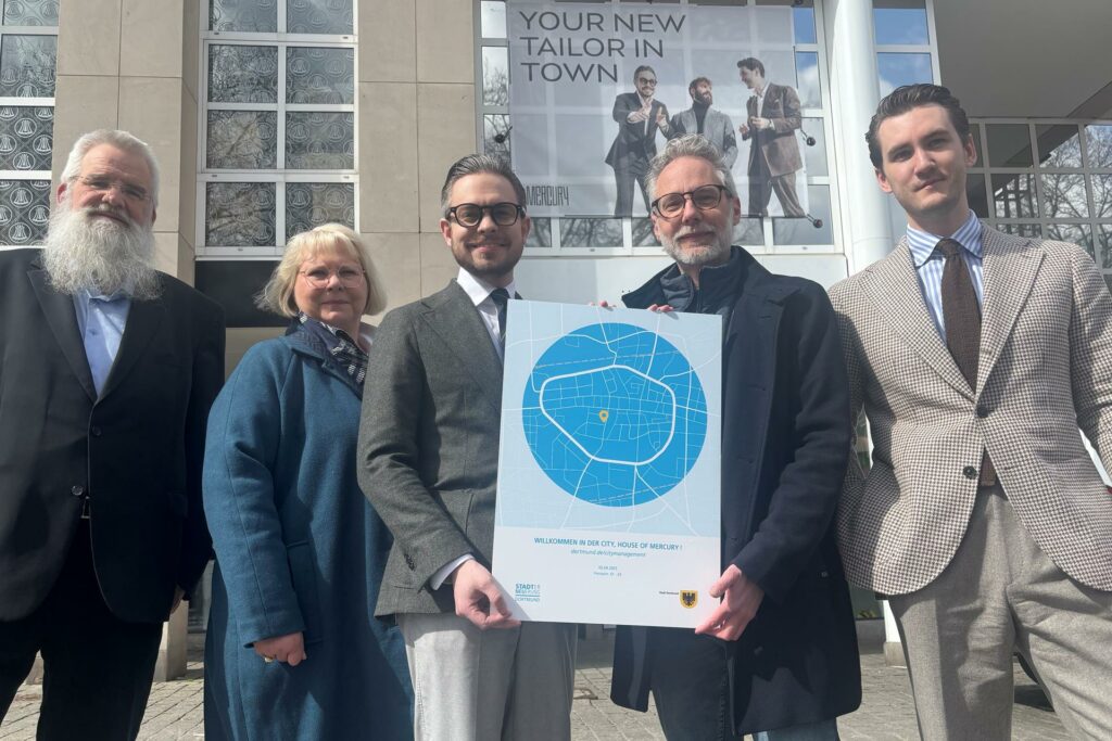 „Willkommen in der City, House of Mercury!“ steht auf der Tafel, die Citymanager Tilmann Insinger (2.v.r.) zur Eröffnung ihres neuen Geschäfts an Pablo Bachmann (Mitte) und Felix Würfel (r.) überreichte. Dabei waren auch Thomas Tiemann (l.) als Vertreter der Propstei-Gemeinde und Anja Borrmann (2.v.l.), Firmenberaterin bei der städtischen Wirtschaftsförderung.