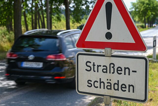 Ein Verkehrsschild warnt vor Straßenschäden. Im Hintergrund ist ein Auto zu sehen.