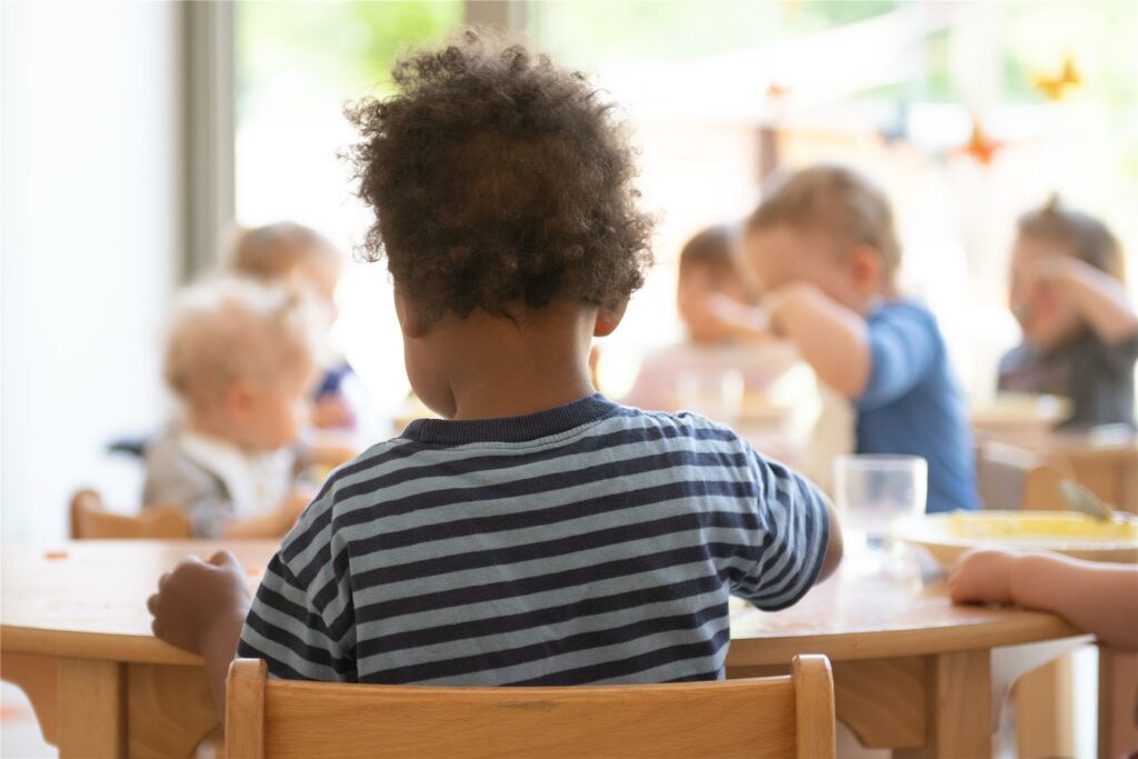 Die Kinder einer Kindergrippe sitzen im Rahmen der Notbetreuung während des Mittagessens an einem Tisch.