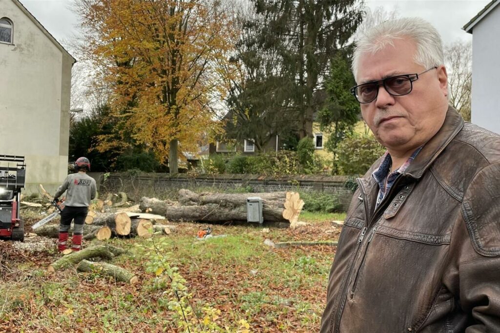 Uwe Paulukat steht vor der ehemaligen Grundschule in Dortmund Kley. Bauarbeiter fällen gerade Kastanien.