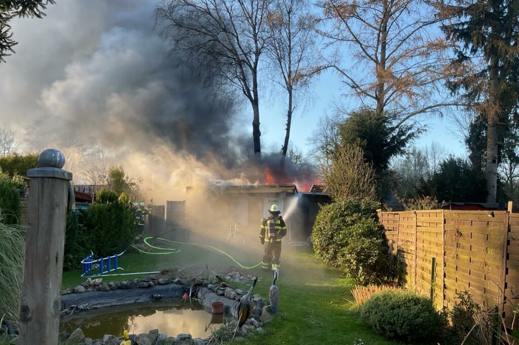 Ein Feuerwehrmann löscht eine brennende Gartenlaube in Dortmund-Menglinghausen