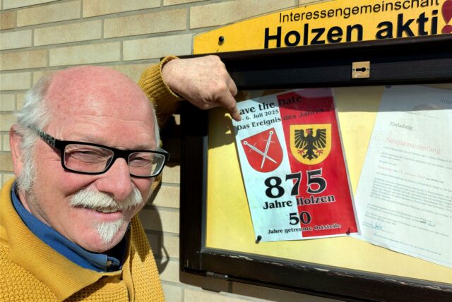 Ein Mann zeigt auf eine Einladung zu einer Jubiläumsfeier in einem Schaukasten an einer Hauswand.