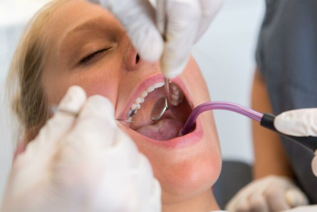 Einer blonden Frau wird beim Zahnarzt der Mundinnenraum kontrolliert.