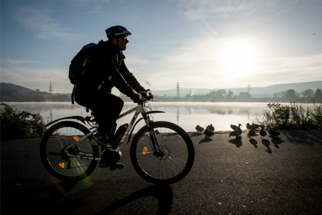 Ein Mountainbiker zeichnet sich am Ufer des Harkortsees als Silhouette im Licht der Morgensonne ab. Der Harkortsee bei der Ortschaft Wetter ist einer der Stauseen der Ruhr.