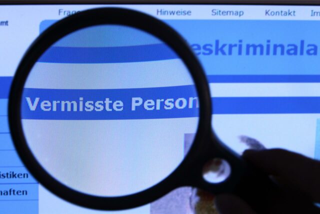 „Vermisste Person“ steht auf einem Computerbildschirm, vor den eine Lupe gehalten wird.
