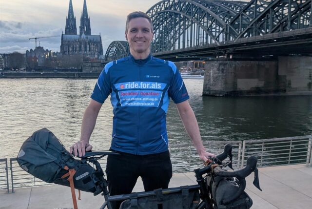 Sebastian Knobloch steht mit seinem Rennrad am Ufer des Rheins in Köln