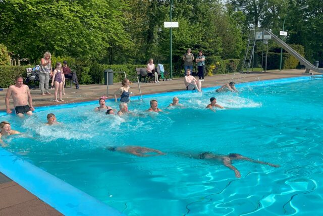 Mehrere Menschen sind im Schwimmbecken des Freibad Derne. Zwei Tauchen. Einige stehen drum herum.