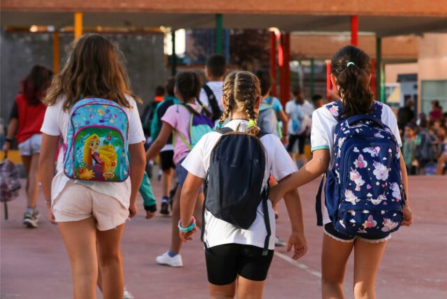 Drei Mädchen mit Schulrucksäcken gehen auf ein Schulgebäude zu.