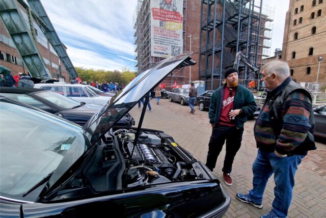 Zwei Autofans unterhalten sich beim Oldtimertreff auf der Hertener Zeche Ewald neben einem schwarzen Fahrzeug mit geöffneter Motorhaube.