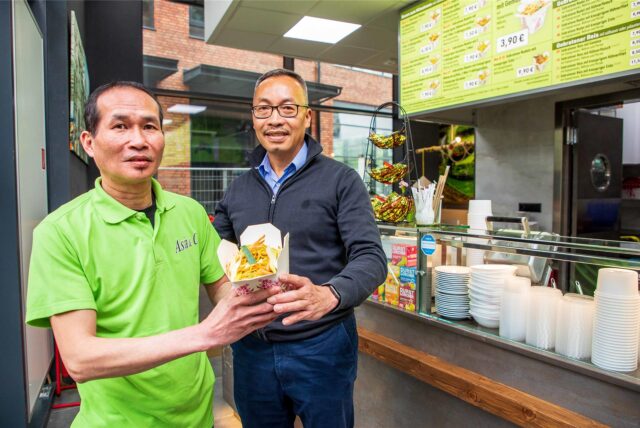 Geschäftsführer Huu Cuong Tran und Hoang Minh Tong stehen im Restaurant Asia & Co. in den Hertener Höfen in Herten und präsentierten eine Box mit gebratenen Nudeln.