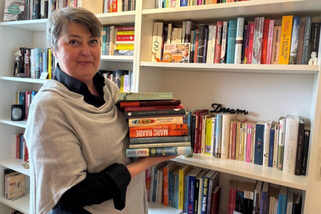 Influencerin Carola Quint von dem Format „Lesen mit Carola“ steht vor einem ihrer vielen Bücherregale, das mit Büchern voll gestellt ist.