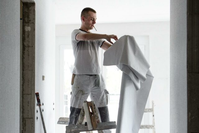 Ein Handwerker tapeziert eine Wohnung.