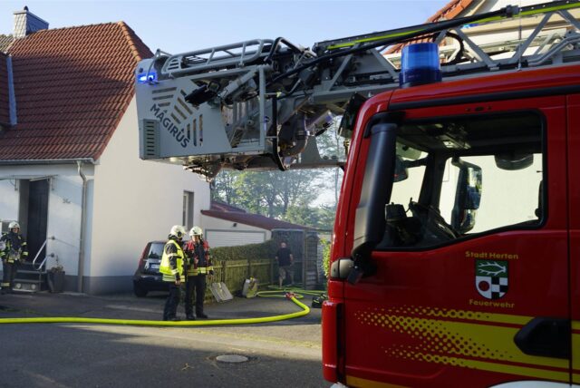 Ein roter Einsatzwagen und mehrere Einsatzkräfte der Berufsfeuerwehr Herten vor einem Wohnhaus in Herten-Bertlich.
