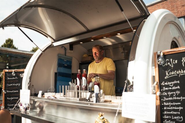 Ein Mann steht in seinem Foodtruck und hält Soßen in seiner Hand.