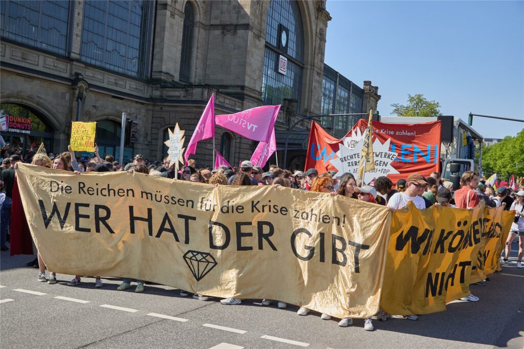 Teilnehmer der Demonstration «Wir haben die Scheiße so satt» vom Bündnis «Wer hat, der gibt» halten am Hamburger Bahnhof Dammtor ein Transparent mit der Aufschrift: «„Die Reichen müssen für die Krise zahlen! Wer hat, der gibt“.
