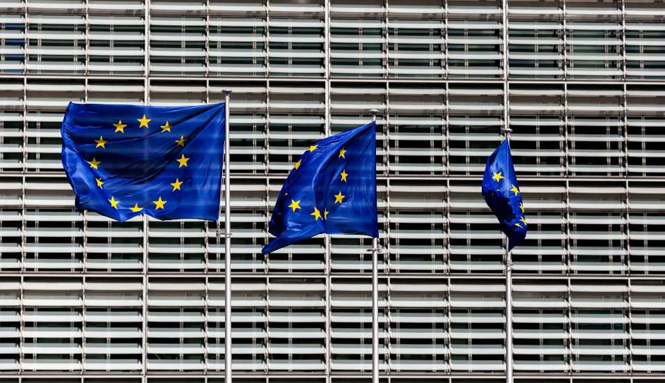 Das Bild zeigt 3 Europa-Flaggen vor einem modernen Gebäudekomplex.