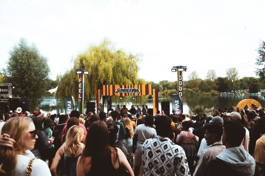 Menschen feiern vor einer bunten Bühne am See bei einem Sommerfestival im Freien in Köln.