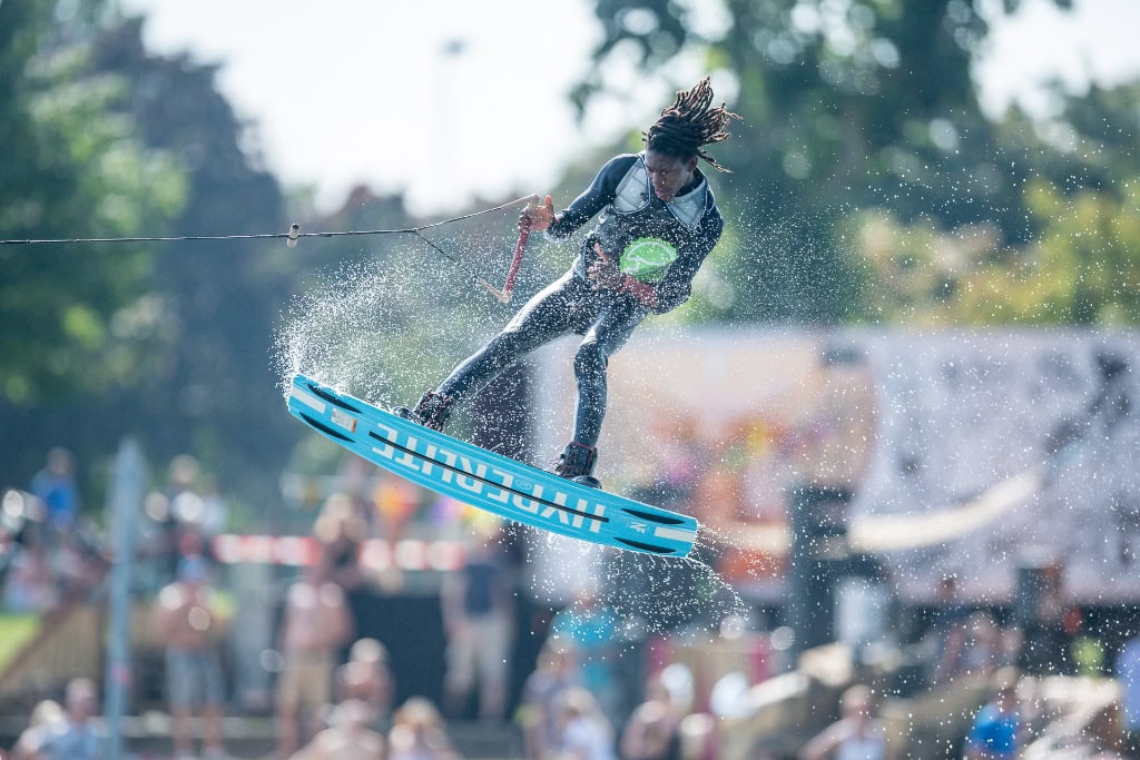 Wakeboarder führt akrobatischen Sprung mit Wasserspritzern bei Sportevent aus.