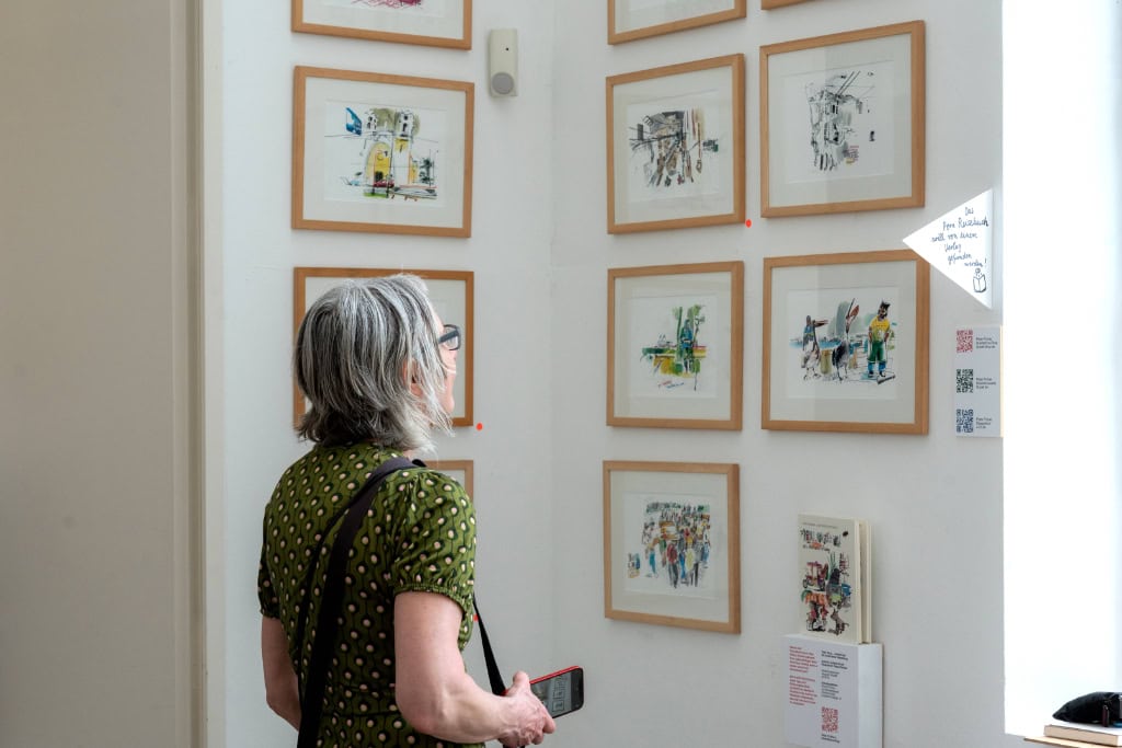 Besucherin betrachtet gerahmte bunte Illustrationen in einer hellen Kunstausstellung.