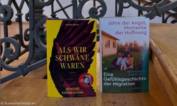 Auf einer Holztreppe stehen zwei Bücher, dahinter ein verschnörkeltes Eisengeländer