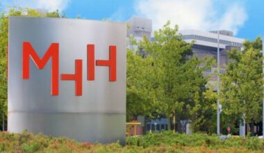 Eine Säule mit den Buchstaben "MHH", im Hintergrund Gebäude.