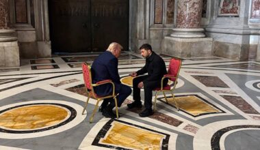 Das Foto zeigt US-Präsident Trump und den ukrainischen Präsidenten Selenskyj im Gespräch miteinander. Beide sitzen sich gegenüber auf goldenen Stühlen, die mit rotem Stoff bezogen sind.