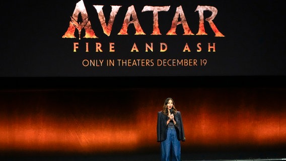 Eine Frau (Zoe Saldaña) steht auf einer Bühne, dahinter stehen auf einer digitalen Leinwand die Worte "Avatar, Fire and Ash" © picture alliance / Chris Pizzello/Invision/AP Foto: Chris Pizzello