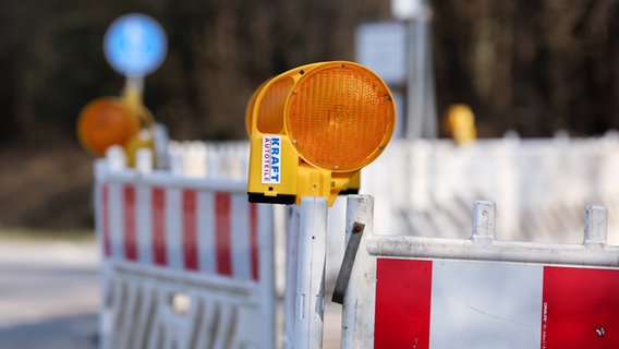 Auf einer Straße stehen mehrere Baustellenzäune, an denen gelbe Baustellenlampen angebracht sind. © NDR Foto: Pavel Stoyan