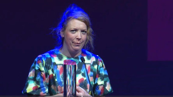 Eine Frau mit hochgesteckten Haaren hält eine Dankesrede für ihren Preis (Lina Beckmann im Ernst-Deutsch Theater) © Screenshot 