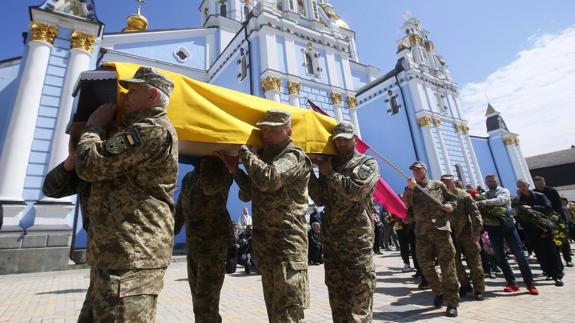Soldaten tragen einen Sarg, der mit einer ukrainischen Flagge bedeckt ist.