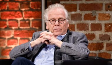 Der frühere Grünen-Politiker und Publizist Daniel Cohn-Bendit (Grüne) im grauen Jacket, hält die Hände verschränkt und sitzt vor einer Ziegelsteinwand.