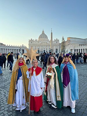 Zwei Mädchen und zwei Jungs stehen in Sternsingerkleidung auf dem Petersplatz in Rom.
