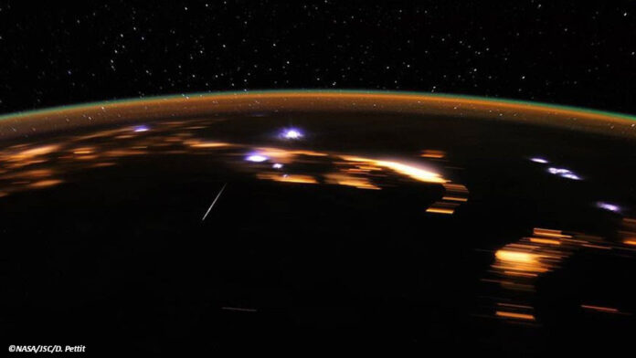 Eine Fotografie vo nder Internationalen Raumstation aus zeigt die Erde bei nacht mit Meteoren der Lyriden.