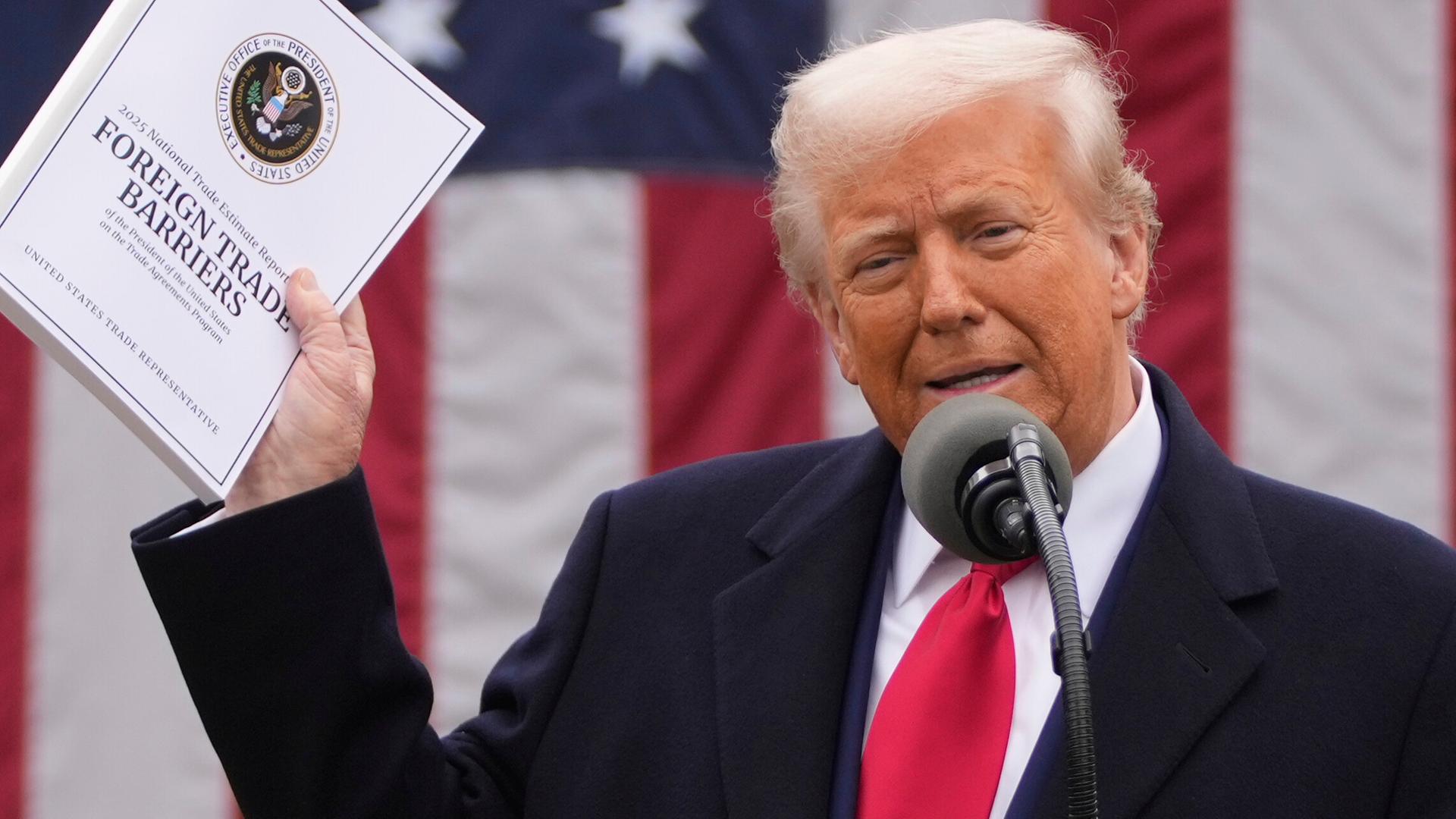 Präsident Trump spricht in im Garten des Weißen Hauses in ein Mikrofon. Er hält eine Mappe mit Zollankündigungen hoch. 2.4.2025